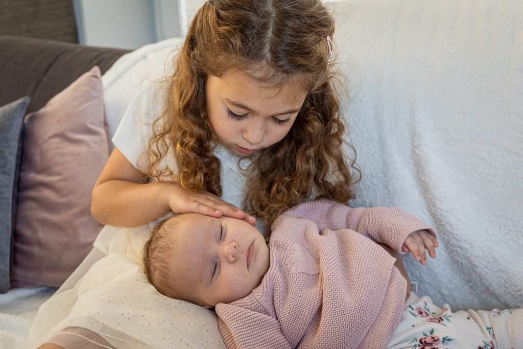 babyfoto mit grosser Schwester im Arm kuscheln